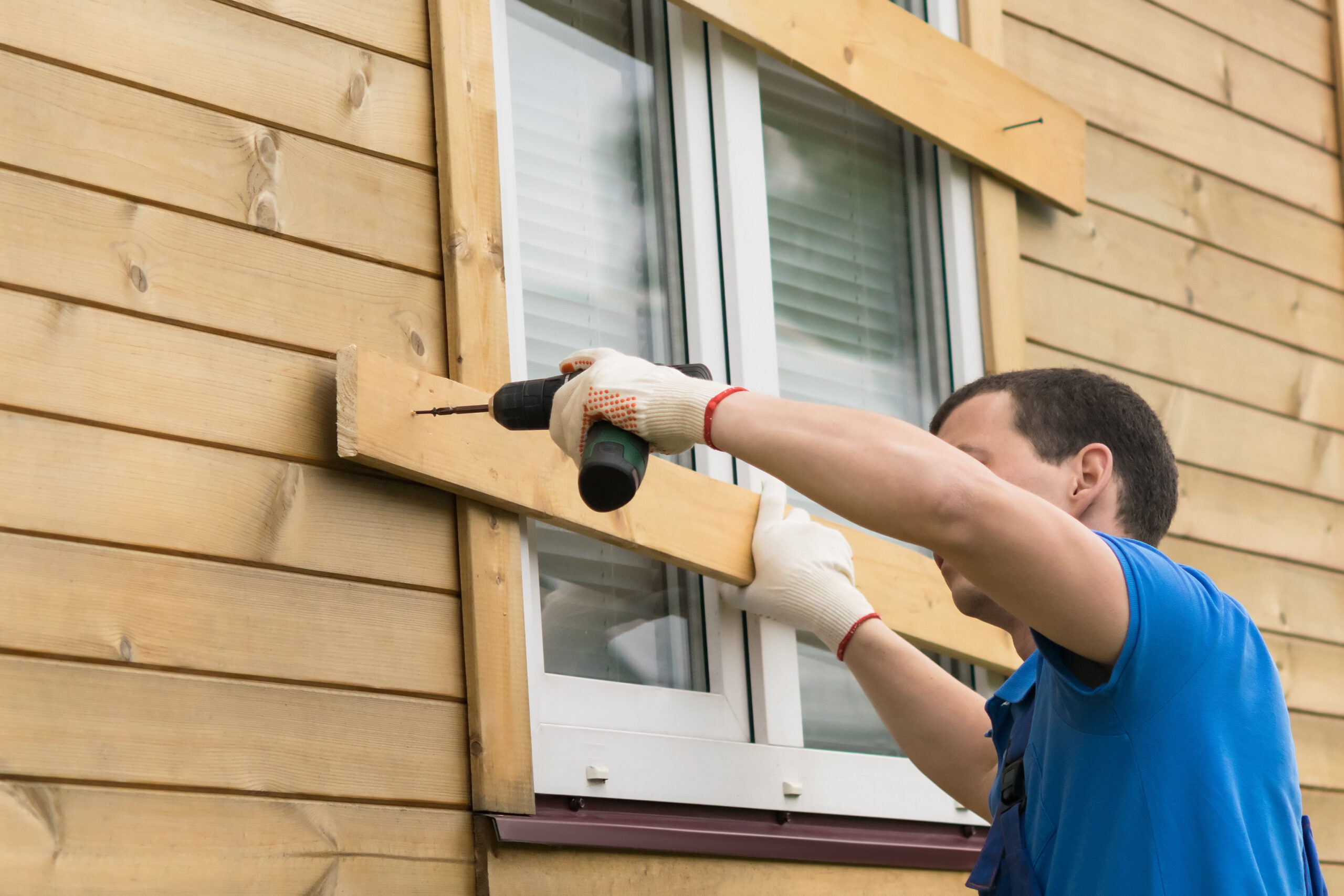 A siding contractor is installing a window on a house using a drill.